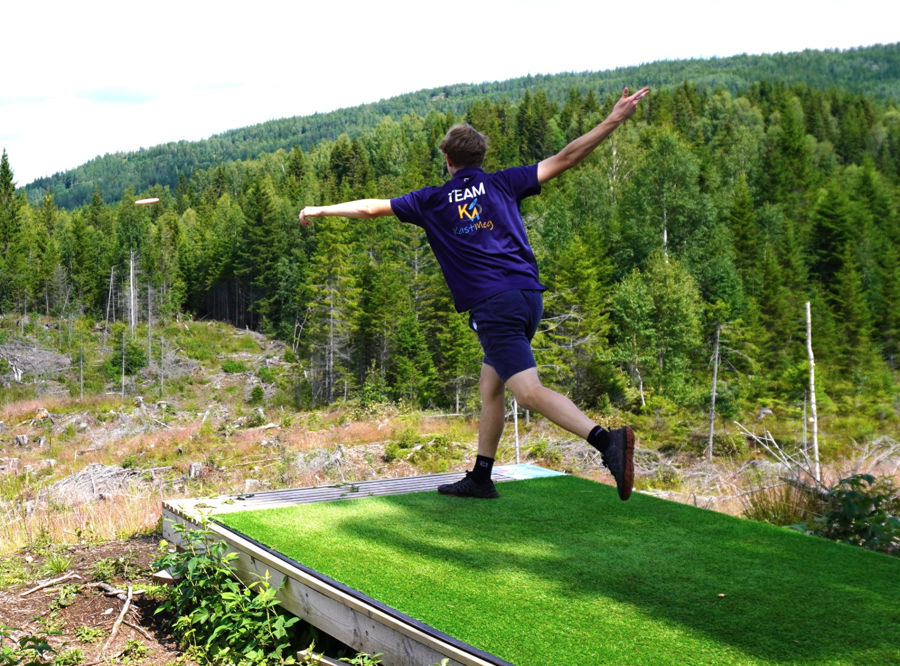 Even Fauskanger fra Team KastMeg i kastbevegelse på discgolf-bane med skog i bakgrunnen